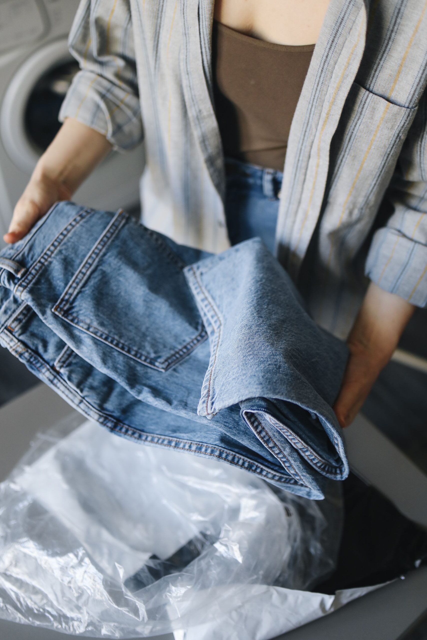 Woman in striped shirt holding folded denim jeans in home laundry setting.